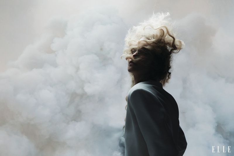 Charlize Theron with tousled blonde hair in profile against a billowy smoke or cloud backdrop for Elle U.S.
