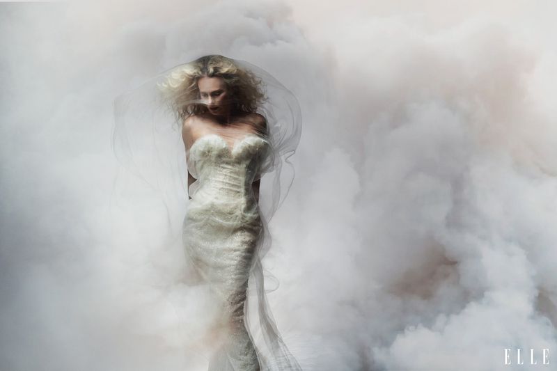 Charlize Theron wearing a strapless white gown amid swirling smoke and tulle for Elle U.S., photographed by Norman Jean Roy.