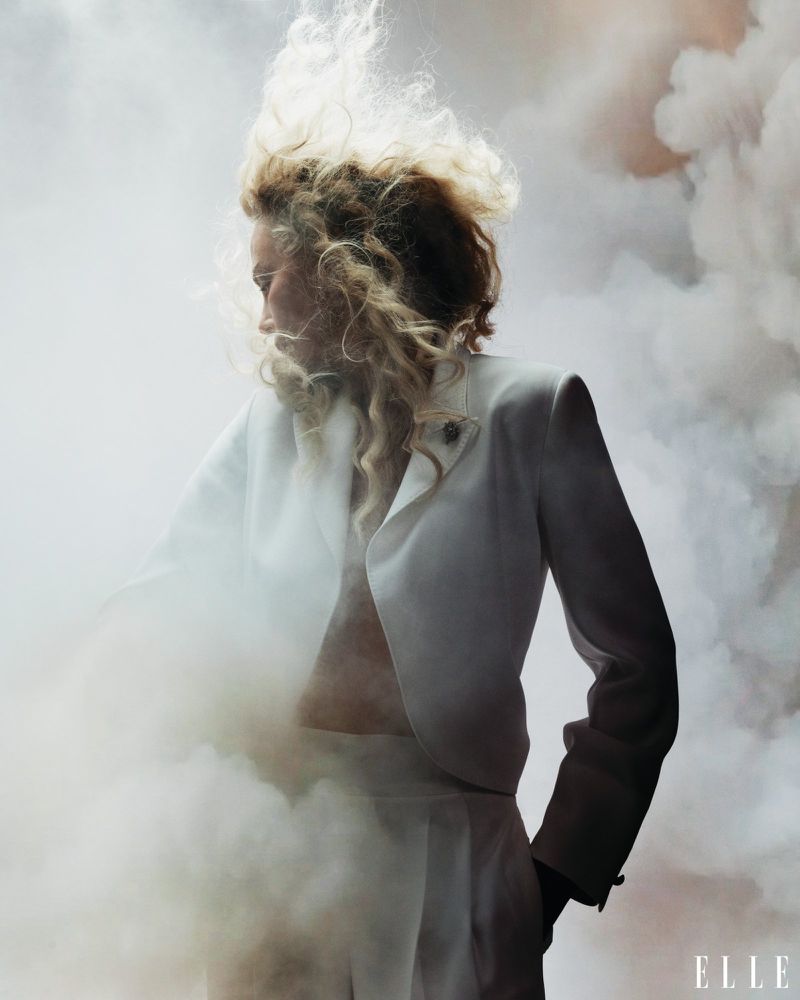 Charlize Theron in a white suit with billowing smoke and tousled blonde hair against a bright background for Elle US.