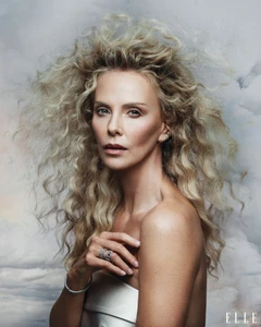 Charlize Theron with voluminous blonde hair against a cloudy sky backdrop for Elle U.S. portrait.