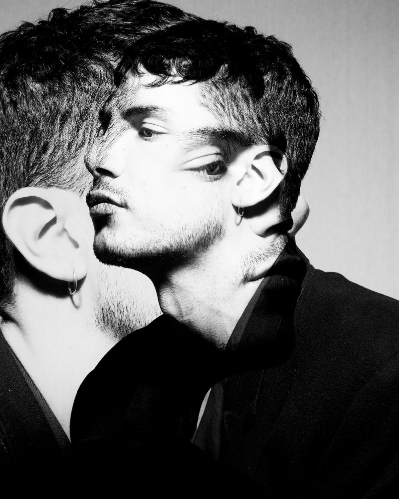 Monochrome multiple exposure portrait of a man with dark hair wearing a black jacket against a plain background