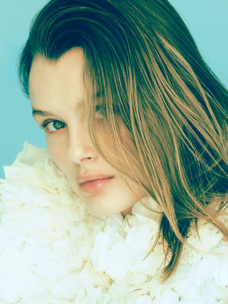 Close up portrait of model Kris Grikaite wearing a white textured ruffled top against a pale blue background