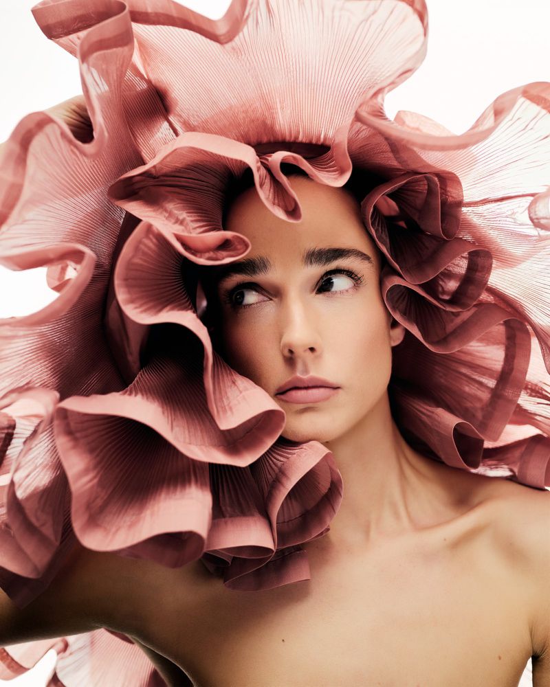 Close-up portrait of a woman wearing an oversized pleated mauve rffled hat for Vogue Portugal Ether Structure editorial