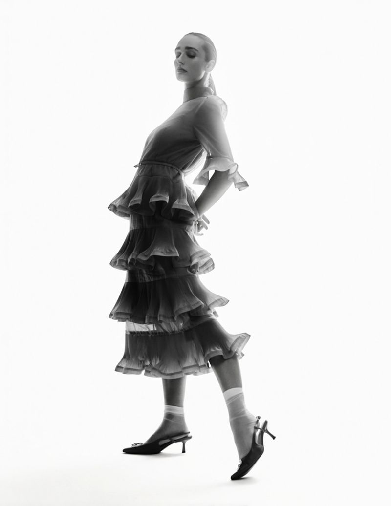 Model wearing a layered tiered dress and slingback heels against a bright white background in a fashion editorial shot.