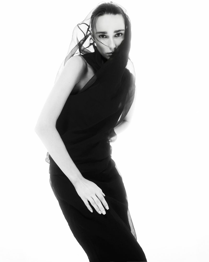 Model wearing a black dress and sheer veil against a white background for Vogue Portugal