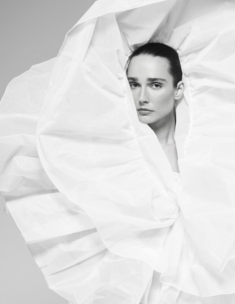 Model framed by an expansive, sculptural white ruffled collar in black and white against a seamless studio background.