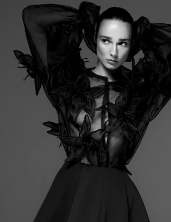 Model in a black sheer floral blouse with voluminous sleeves posing against a dark background for Vogue Portugal.