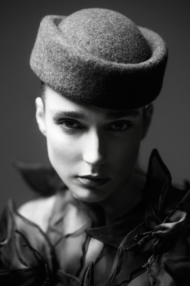 Monochrome portrait of a woman wearing a round felt pillbox hat and dark sculptural ruffled collar.