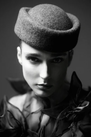 Monochrome portrait of a woman wearing a round felt pillbox hat and dark sculptural ruffled collar.