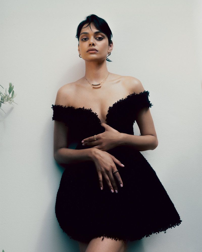 Model Zinnia Kumar posing in a textured off-the-shoulder black mini dress against a pale neutral wall for Elle India.