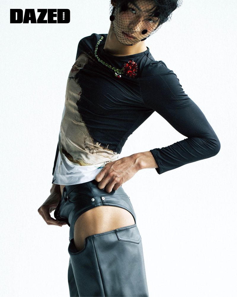 Model wearing a black graphic long sleeve top and dark leather trousers with cut-outs against a plain white background