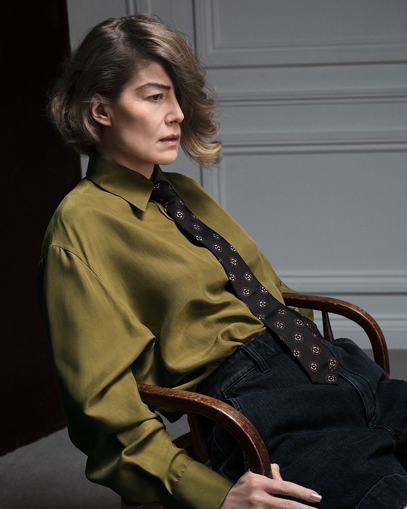 Rosamund Pike seated in a wooden chair wearing an olive green shirt and dark tie for British GQ
