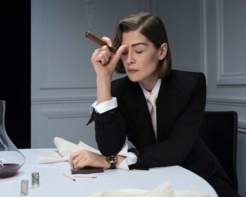 Rosamund Pike in a black suit holding a cigar at a dining table for British GQ