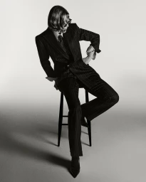 Rosamund Pike seated on a stool wearing a dark pinstripe suit and tie for British GQ