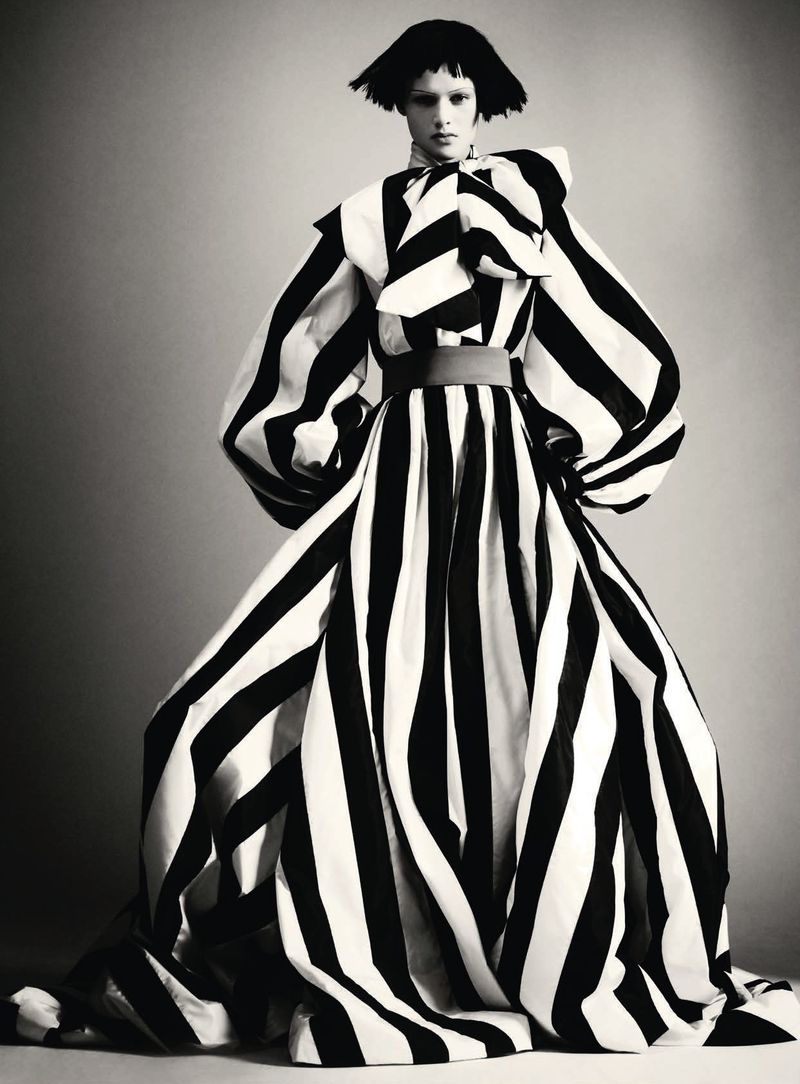 Model wearing a voluminous black and white striped haute couture gown with puffed sleeves against a grey studio backdrop.