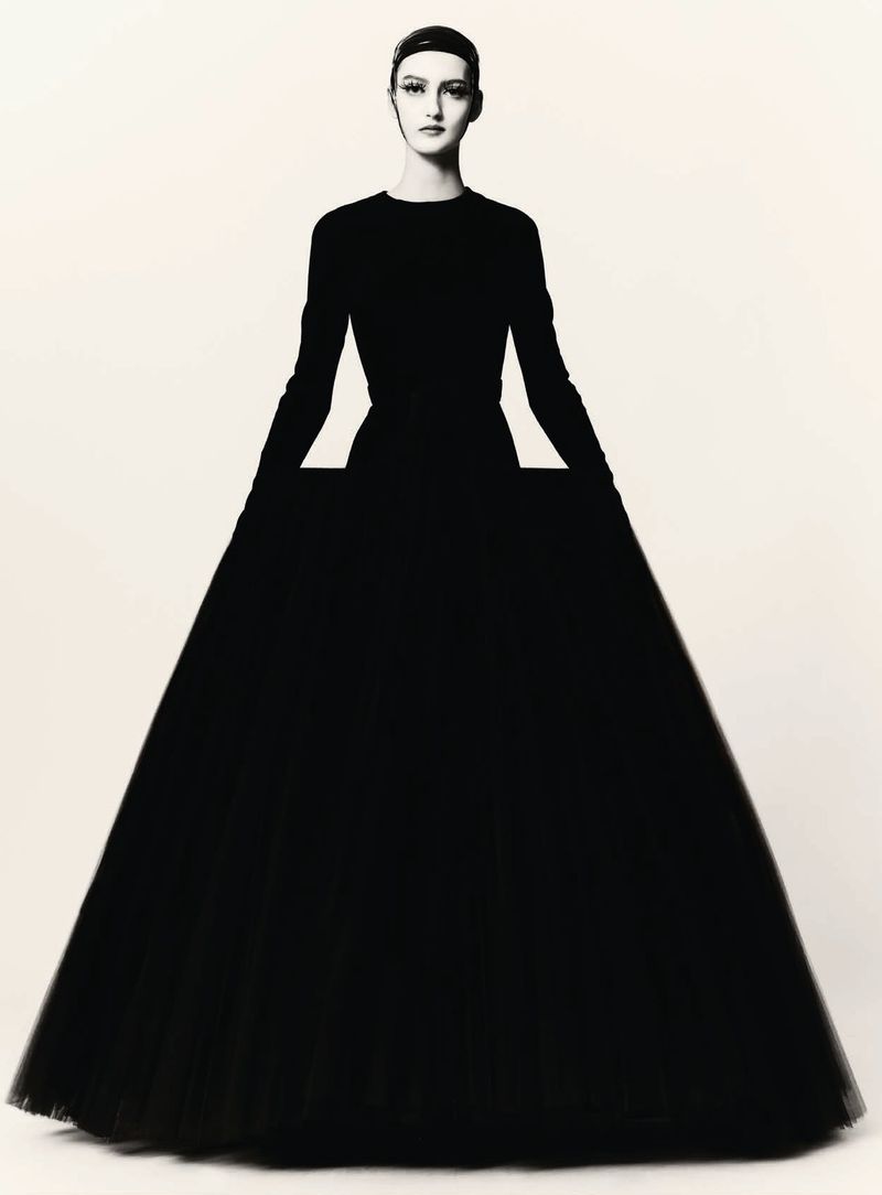 Model in a structured black ballgown wearing a dark cap against a plain white background