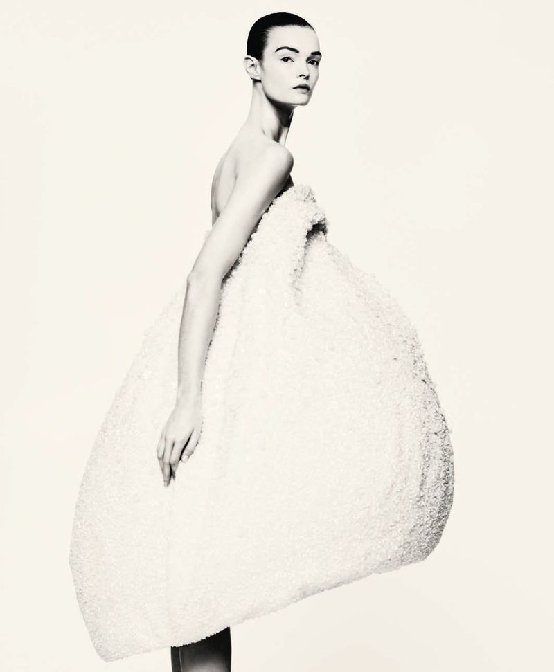 Model wearing a voluminous white textured sculptural dress against a plain light background