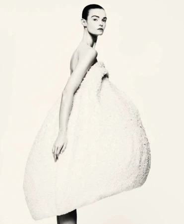 Model wearing a voluminous white textured sculptural dress against a plain light background