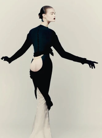 Model in black evening gown with cutout back wearing black gloves against a light background