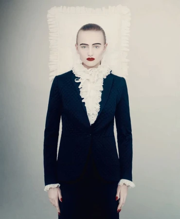 Model in a dark blazer with a ruffled white collar standing before a white backdrop for D Repubblica haute couture