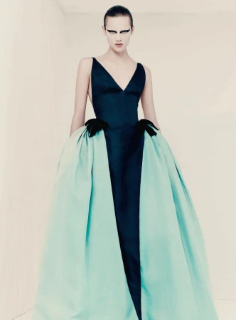 Model posing in a black V-neck column gown with dramatic voluminous mint green side bustles and bold winged black eye makeup.