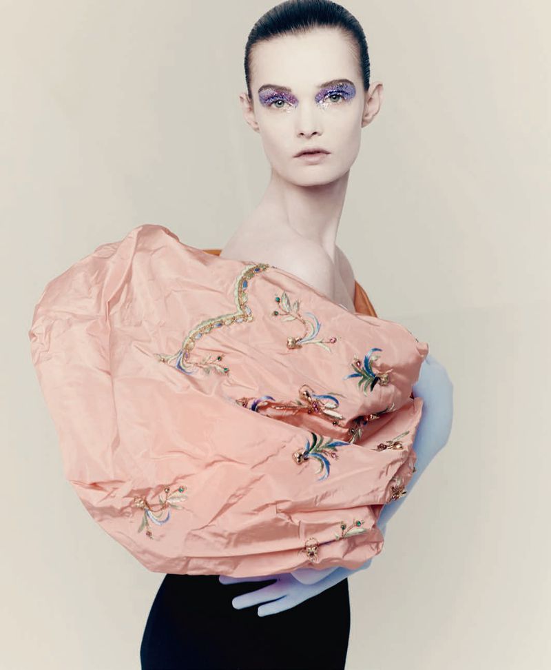 Model Lulu Tenney posing in an embroidered voluminous peach top with a blue opera glove against a plain studio background.
