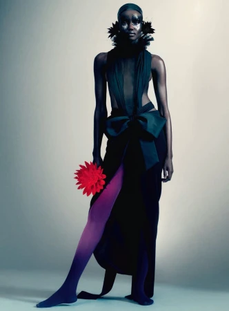 Model in dark gown with large bow holding a red flower against a neutral gradient background