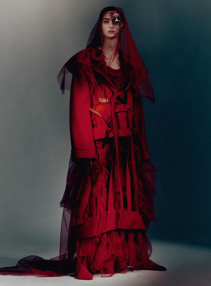 Model in red Haute Couture gown and sheer veil standing in moody studio light for D Repubblica by Paolo Roversi.
