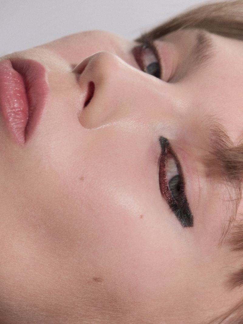 Extreme close-up beauty shot of a model featuring graphic winged black eyeliner, glossy mauve lips, and clean skin texture.