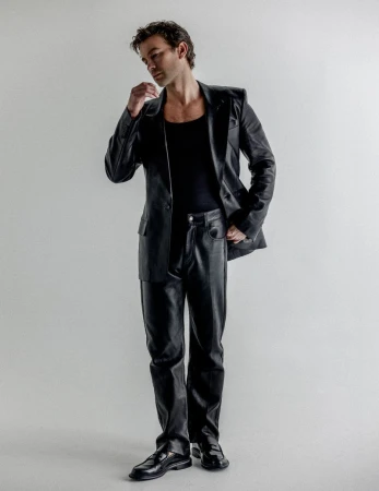 Full-length portrait of Chace Crawford wearing a black leather blazer and matching pants against a plain studio background.