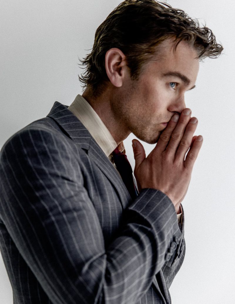 Profile portrait of actor Chace Crawford wearing a grey pinstripe suit and light yellow shirt with hands clasped near face