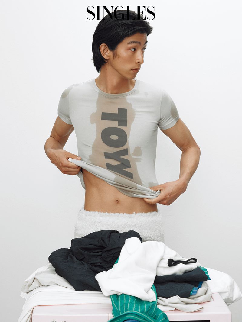 Yugo Takano lifting a graphic grey t-shirt over a pile of laundry against a white background for Singles Magazine.