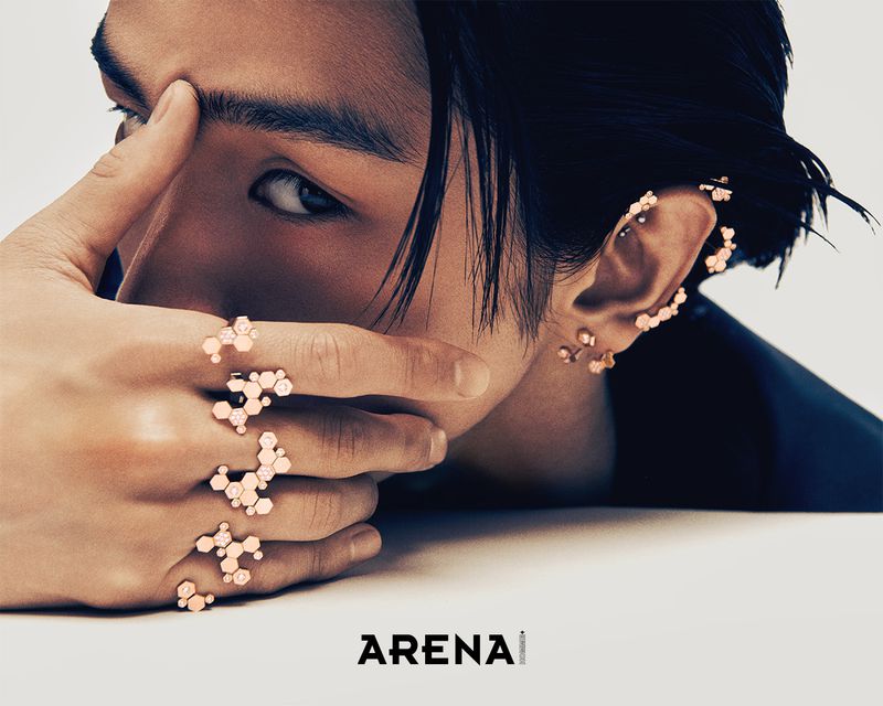 Close-up portrait of a male model wearing gold honeycomb rings and ear cuffs against a light background