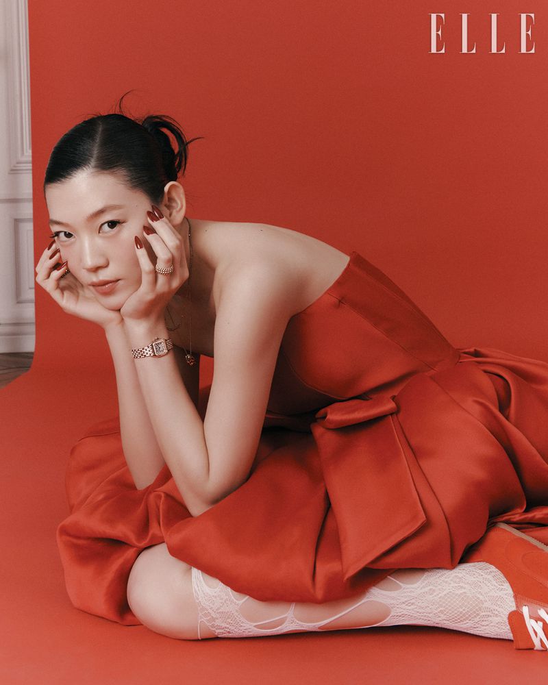 Elegant woman in a red strapless dress and lace stockings poses against a matching red backdrop for an indoor fashion editorial.