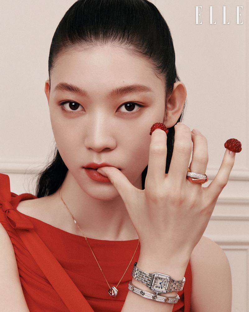 Asian woman in red dress and rings poses indoors for beauty fashion shoot. Jewelry details include a silver watch and necklace.
