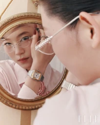 Model wearing glasses and a metallic watch looking into an ornate round gold mirror, photographed by Go Wontae for Elle Korea.