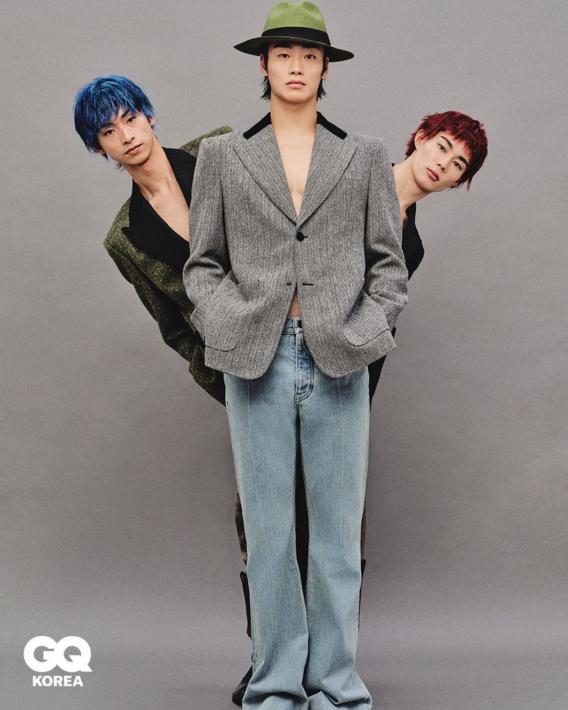 Three young men posing together against a plain grey background for GQ Korea, featuring styled hair and fashion attire.