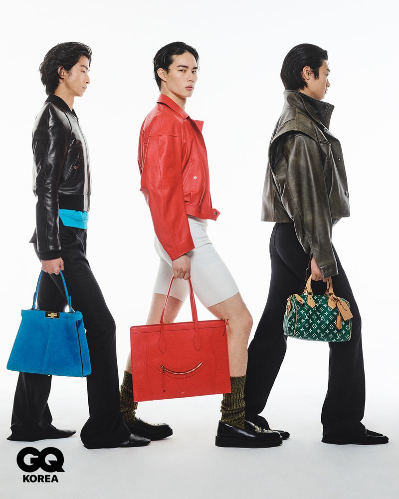 Three male models in leather jackets walking in profile carrying designer handbags against a clean white seamless studio background.
