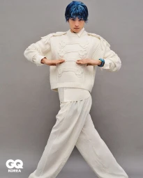 Model Yugo Takano with blue hair wearing a cream military-style knit sweater and wide-leg trousers against a grey backdrop for GQ Korea.