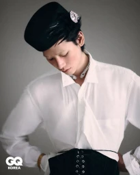 Model Yugo Takano wearing a white button-down shirt, black lace-up corset belt, and jeweled black beret against a grey background.