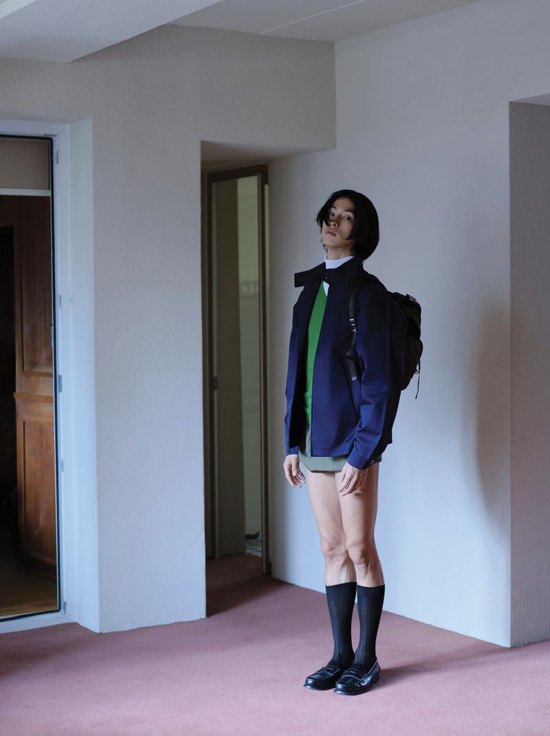 Model Yugo Takano in a dark jacket, green top, and shorts standing indoors on pink carpet for Esquire Korea.