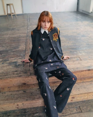 Model sitting on wooden steps wearing an embroidered denim set and varsity jacket for the Kenzo Pre-Spring 2027 collection.