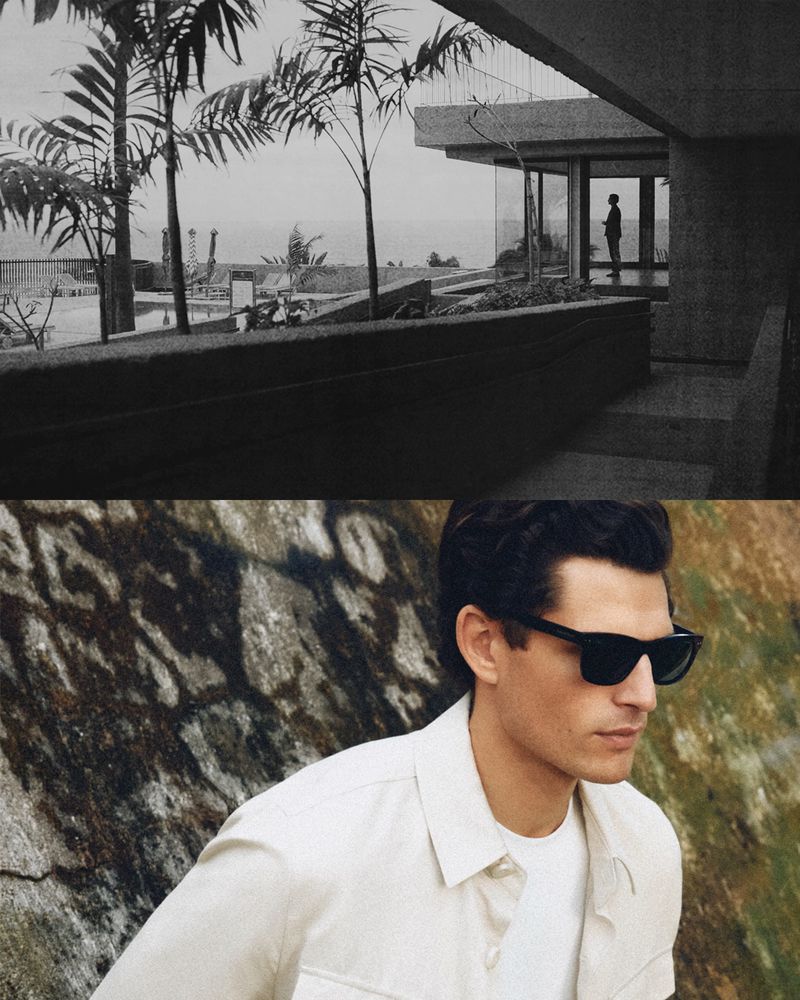 Man wearing sunglasses and a white shirt against a textured stone wall, with an architectural landscape view above.