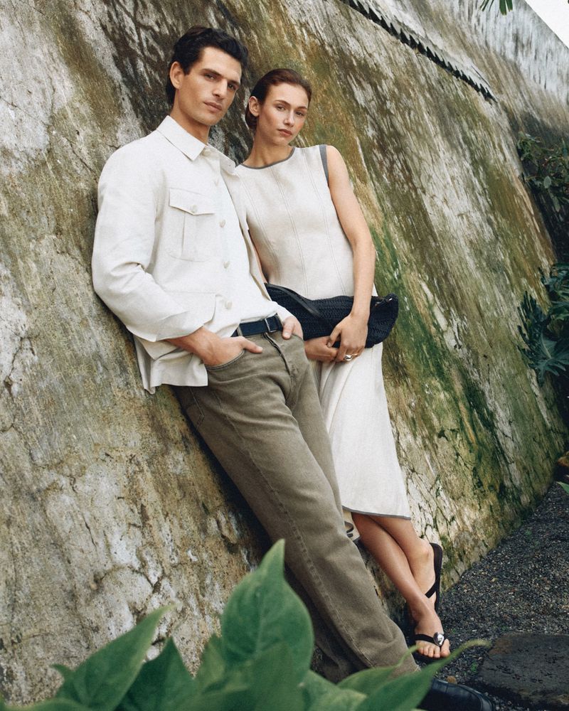 A man and a woman posing outdoors, leaning against a weathered stone wall for the Pedro del Hierro campaign.