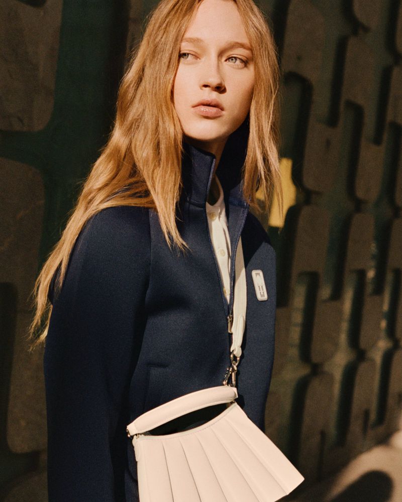 Model Elise Marie wears a navy high-collar zip jacket and pleated off-white crossbody bag for Lacoste Tennis Attitude.