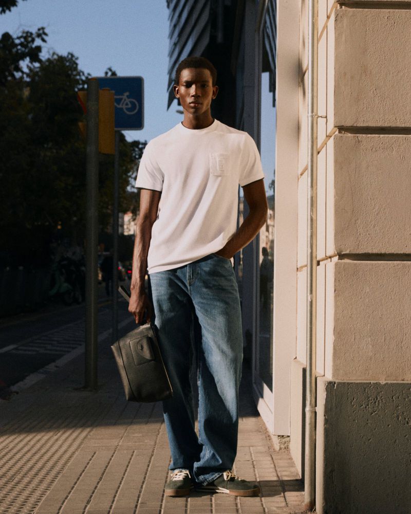 Model wearing a white t-shirt and blue jeans holding a black bag on a city street