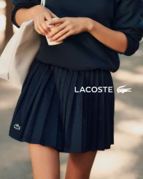 Model wearing a navy pleated skirt and sweatshirt holding a cup and white bag for Lacoste Tennis Attitude Spring 2026