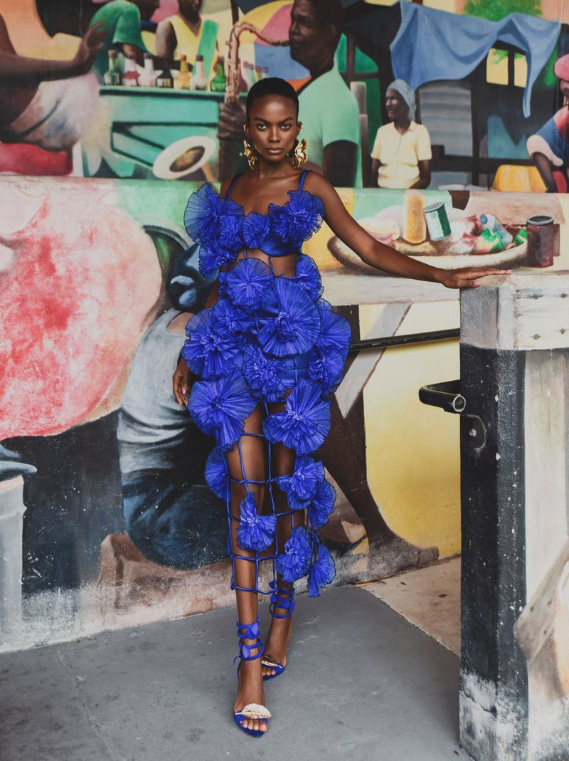 Model in vibrant blue ruffled dress and matching lace-up heels standing in front of a colourful painted wall mural.