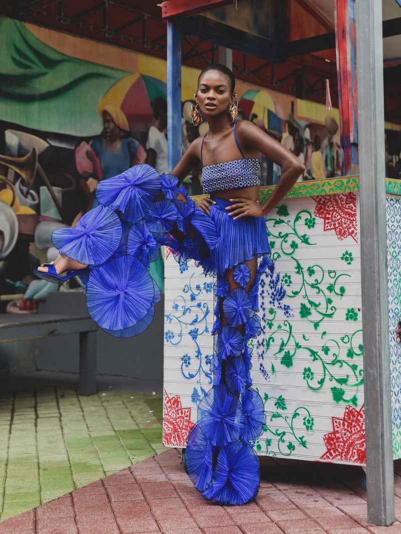 Model in cobalt blue patterned two-piece outfit with elaborate ruffled tulle pant legs posing outdoors.
