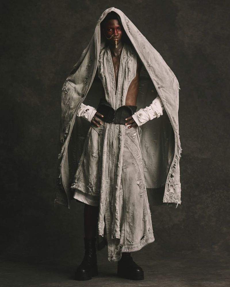 Model Matthieu Akpo wearing a distressed grey hooded denim outfit with a black corset belt in the JULIUS Spring/Summer 2026 lookbook.